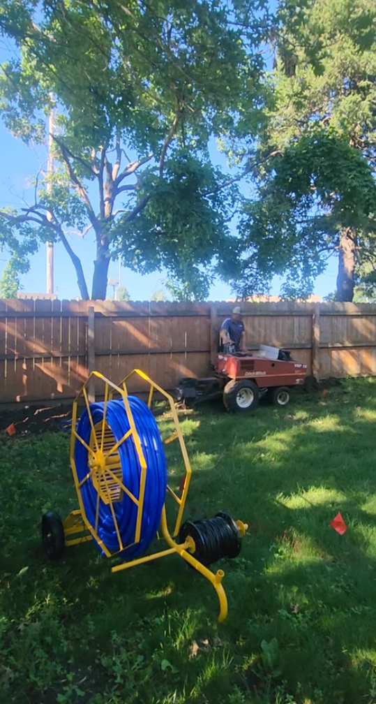 Blue and yellow hose reel on grass with a person and machine in the background