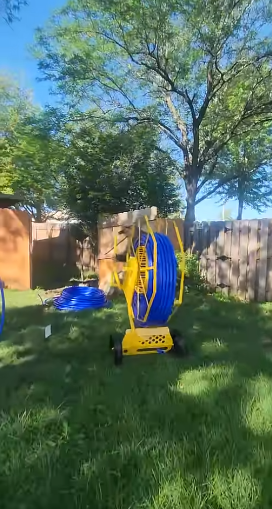 Yellow hose reel with blue hose on a grassy lawn with trees in the background
